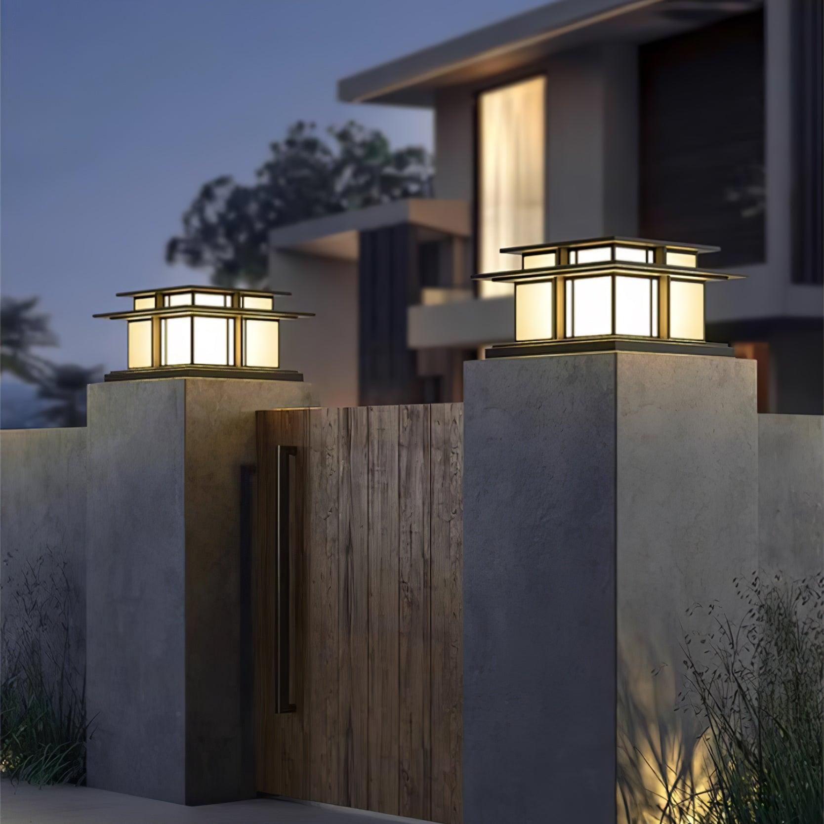 Two Clérachic Ray pillar lights lit on concrete gate piers outside a modern house at dusk.