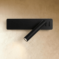 Clérachic matte black wall reading light with a rectangular backplate and an angled cylindrical arm, lit on a plaster wall.