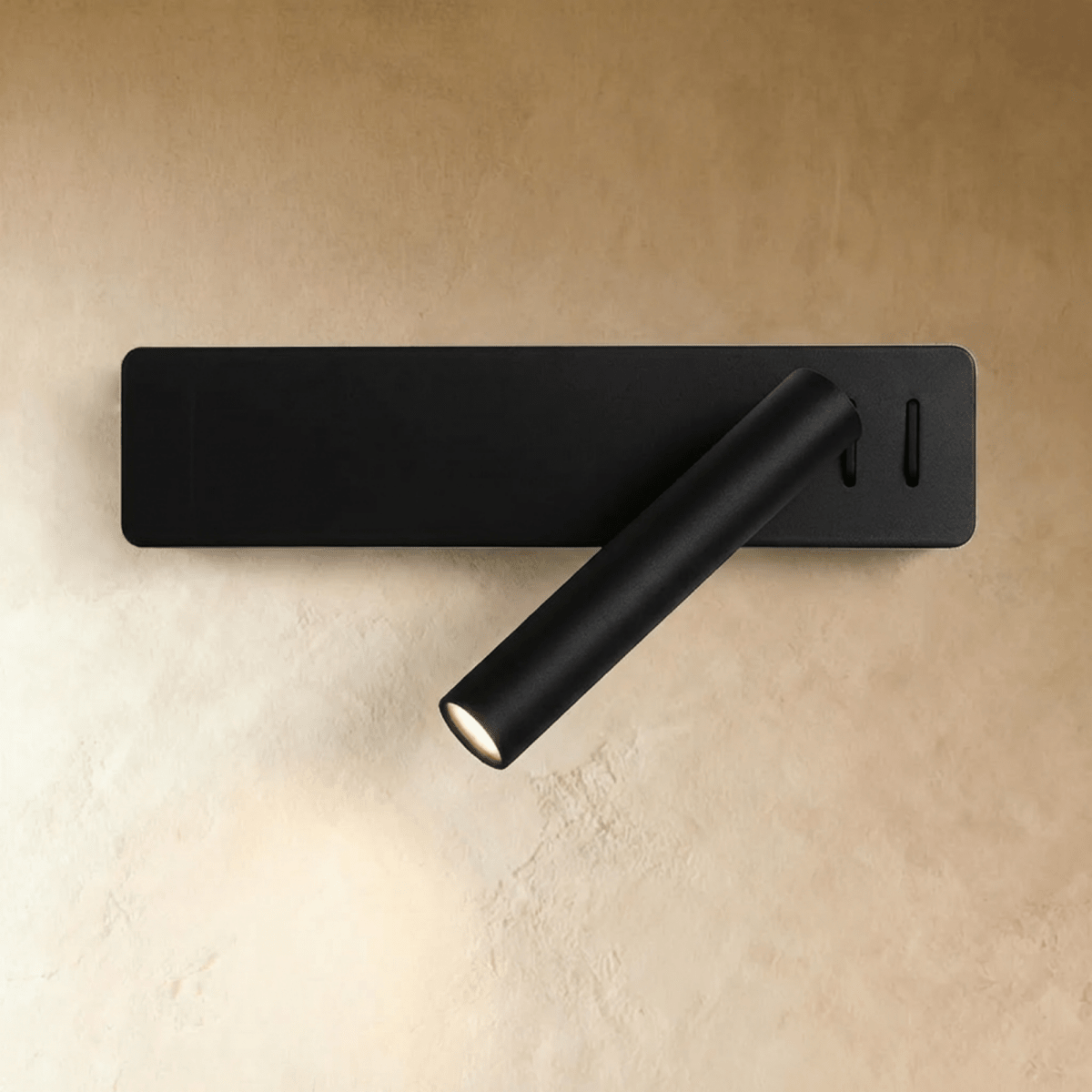 Clérachic matte black wall reading light with a rectangular backplate and an angled cylindrical arm, lit on a plaster wall.