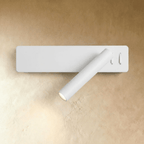 Clérachic white wall reading light with a slim rectangular backplate and angled cylindrical arm, glowing against a plaster wall.