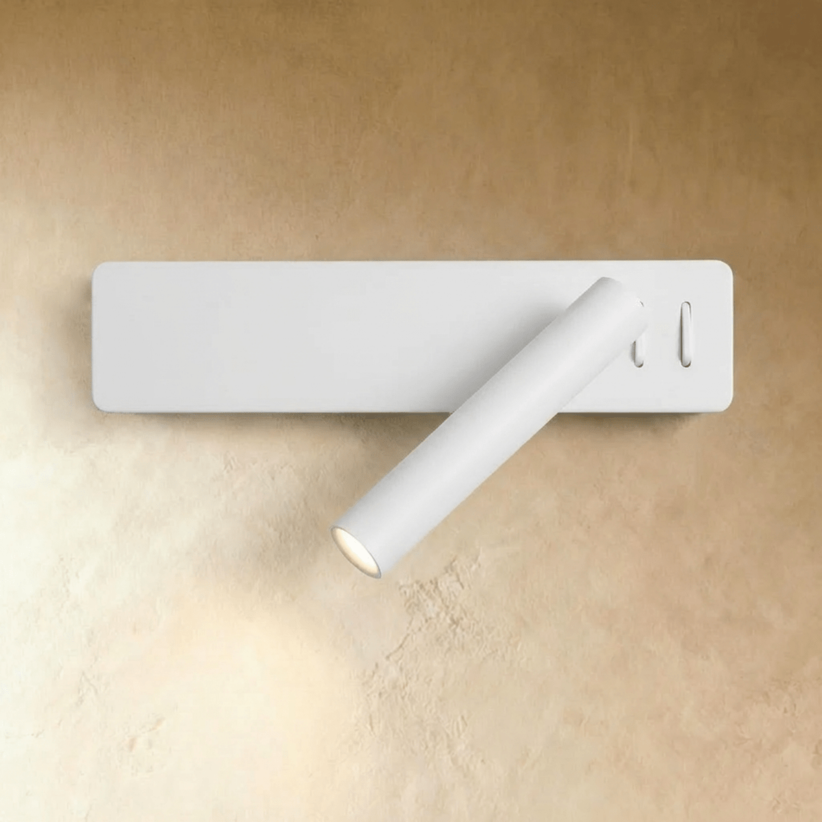 Clérachic white wall reading light with a slim rectangular backplate and angled cylindrical arm, glowing against a plaster wall.