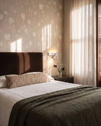 Clérachic white reading wall light beside a bed with a brown headboard, floral wallpaper and sheer curtains in morning light.