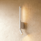 Clérachic slim white wall light with a vertical glowing LED strip and a small pivoting reading spot, on a limewash wall.