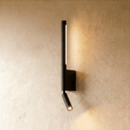 Clérachic slim black wall light with a lit vertical LED strip and a small angled reading spot on a plaster wall.