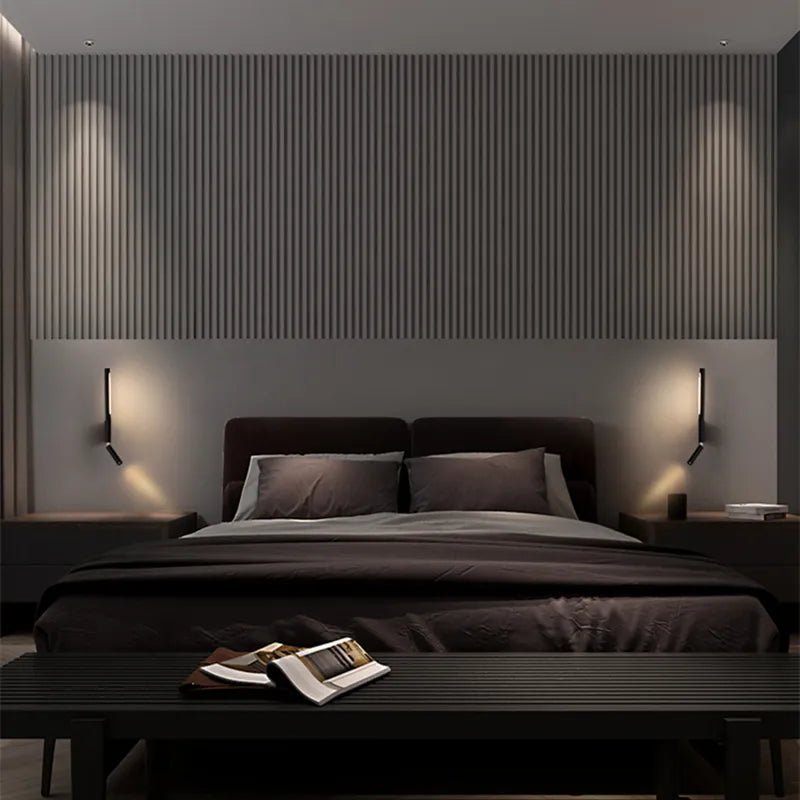 Pair of Clérachic slim black wall lights with reading spots flanking a dark bed against a fluted wall panel in a dim bedroom.