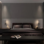 Pair of Clérachic slim black wall lights with reading spots flanking a dark bed against a fluted wall panel in a dim bedroom.