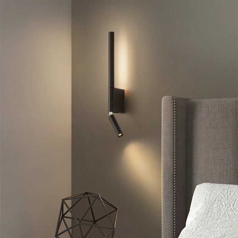 Clérachic slim black wall light with a warm vertical glow and a downward reading spot beside a grey studded headboard.