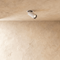 Clérachic recessed spotlight in white, its cylindrical head angled out of a round trim on a limewashed plaster ceiling, lit.