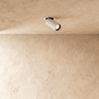 Clérachic recessed spotlight in white, its cylindrical head angled out of a round trim on a limewashed plaster ceiling, lit.