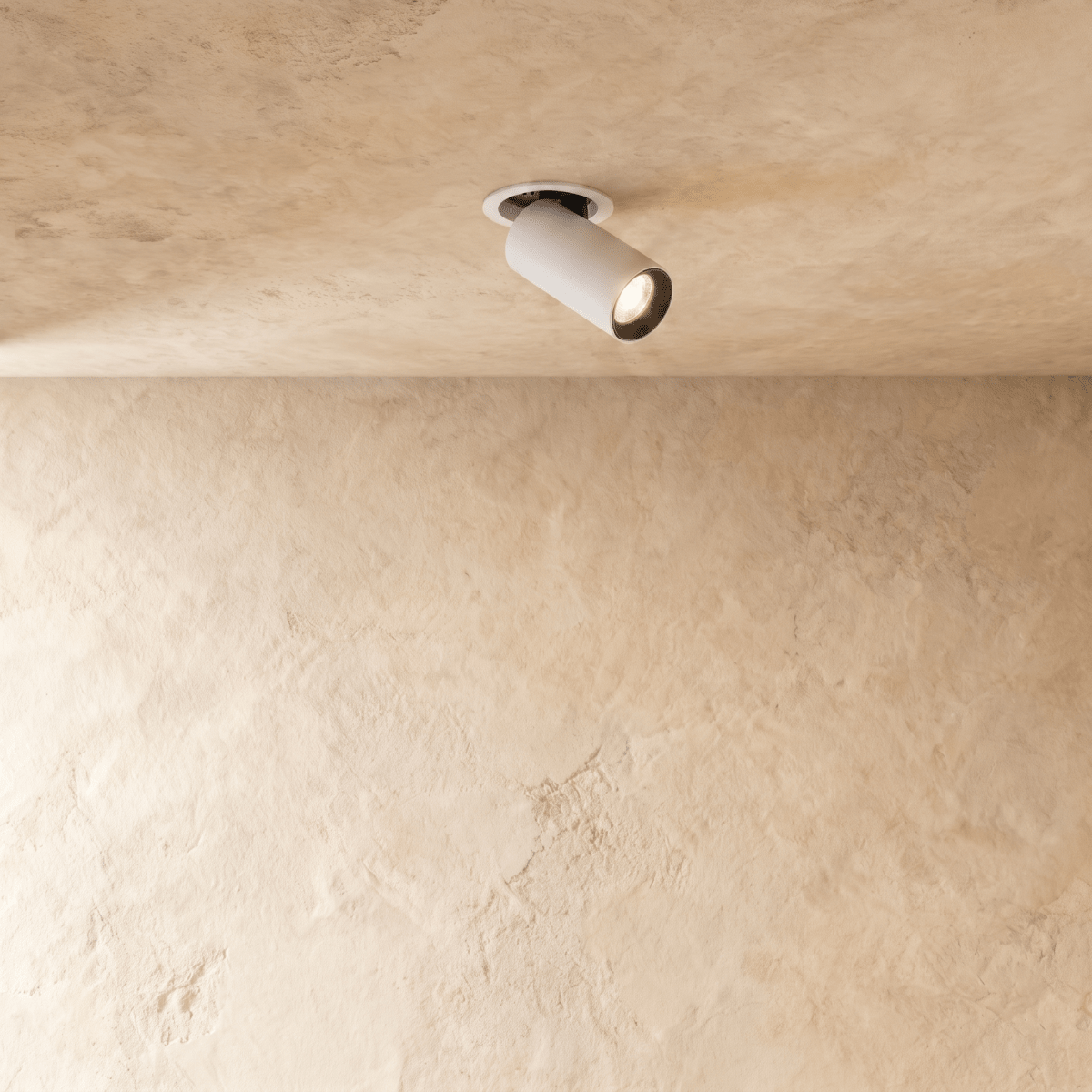 Clérachic recessed spotlight in white, its cylindrical head angled out of a round trim on a limewashed plaster ceiling, lit.