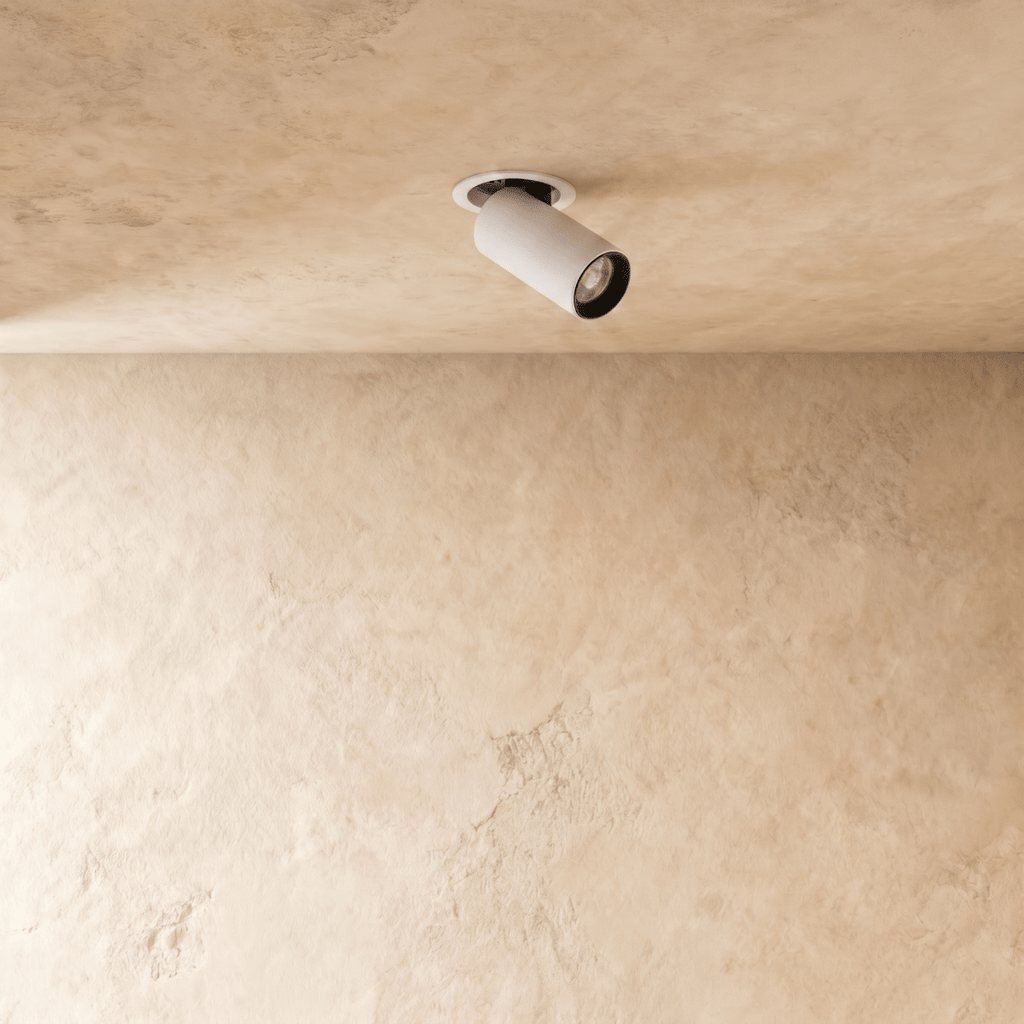 Clérachic white recessed downlight with a black-lined cylindrical head pivoted from a round flush trim on a textured plaster ceiling.