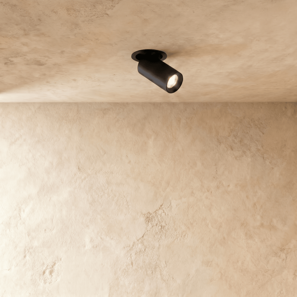 Clérachic recessed downlight in matt black, the pivoting cylindrical head glowing warm against a pale limewashed plaster ceiling.