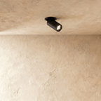 Clérachic recessed downlight in matt black, the pivoting cylindrical head glowing warm against a pale limewashed plaster ceiling.