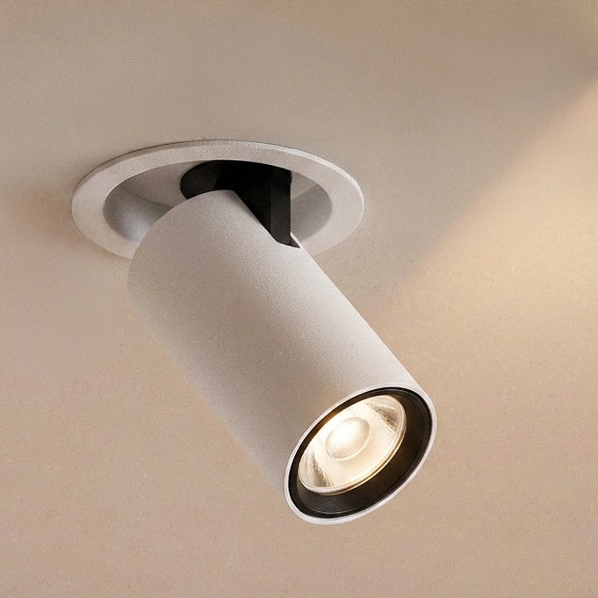 Close view of a Clérachic white recessed downlight, cylindrical head tilted from a round trim, black inner ring and warm beam.