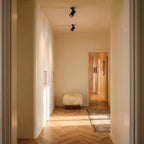 Clérachic black spotlights lighting a warm hallway with herringbone parquet, a sheepskin stool and cream curved cabinets.