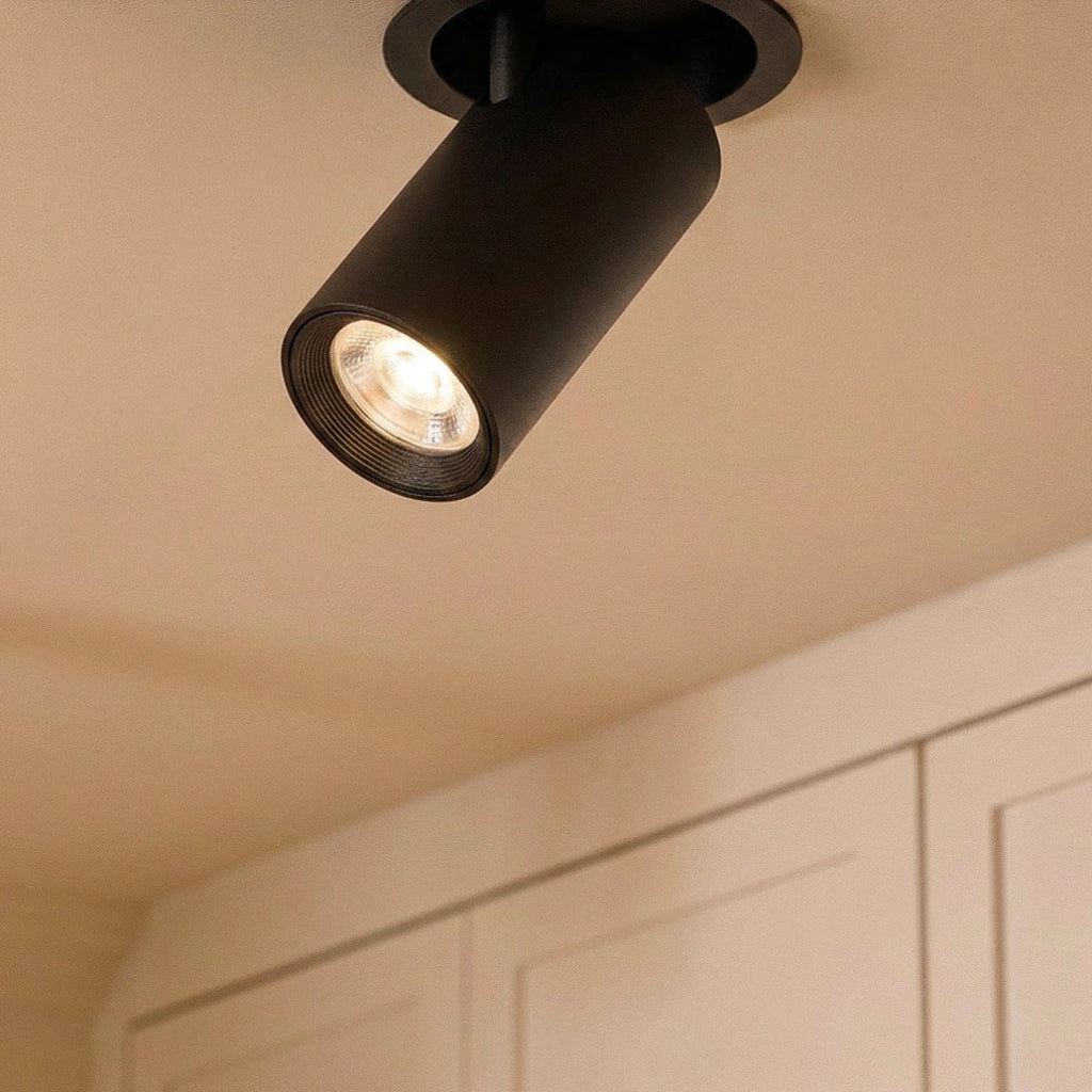 Clérachic black cylindrical spotlight head angled from a round recessed trim, ribbed inner reflector lit warm above cabinets.