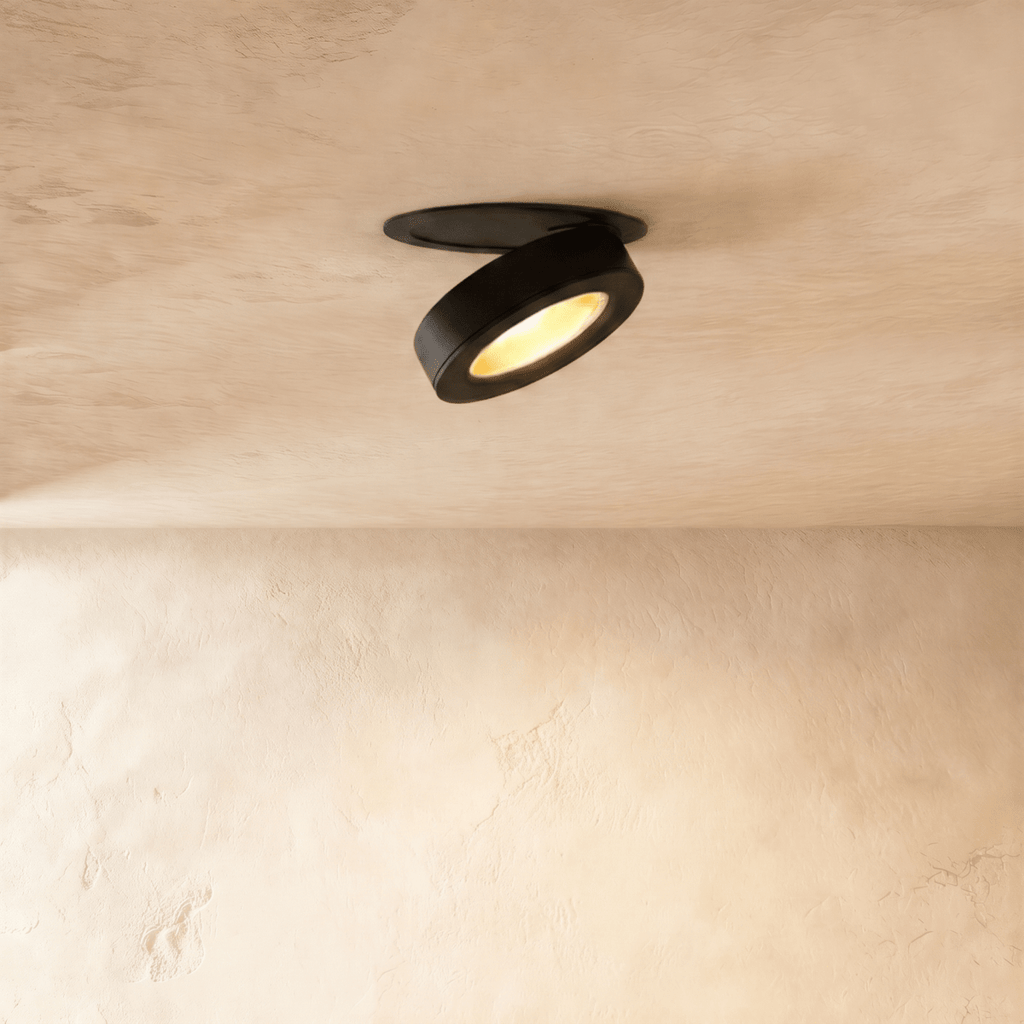 Clérachic recessed downlight in black, head swung down out of its ceiling plate and lit warm against a pale limewash ceiling.