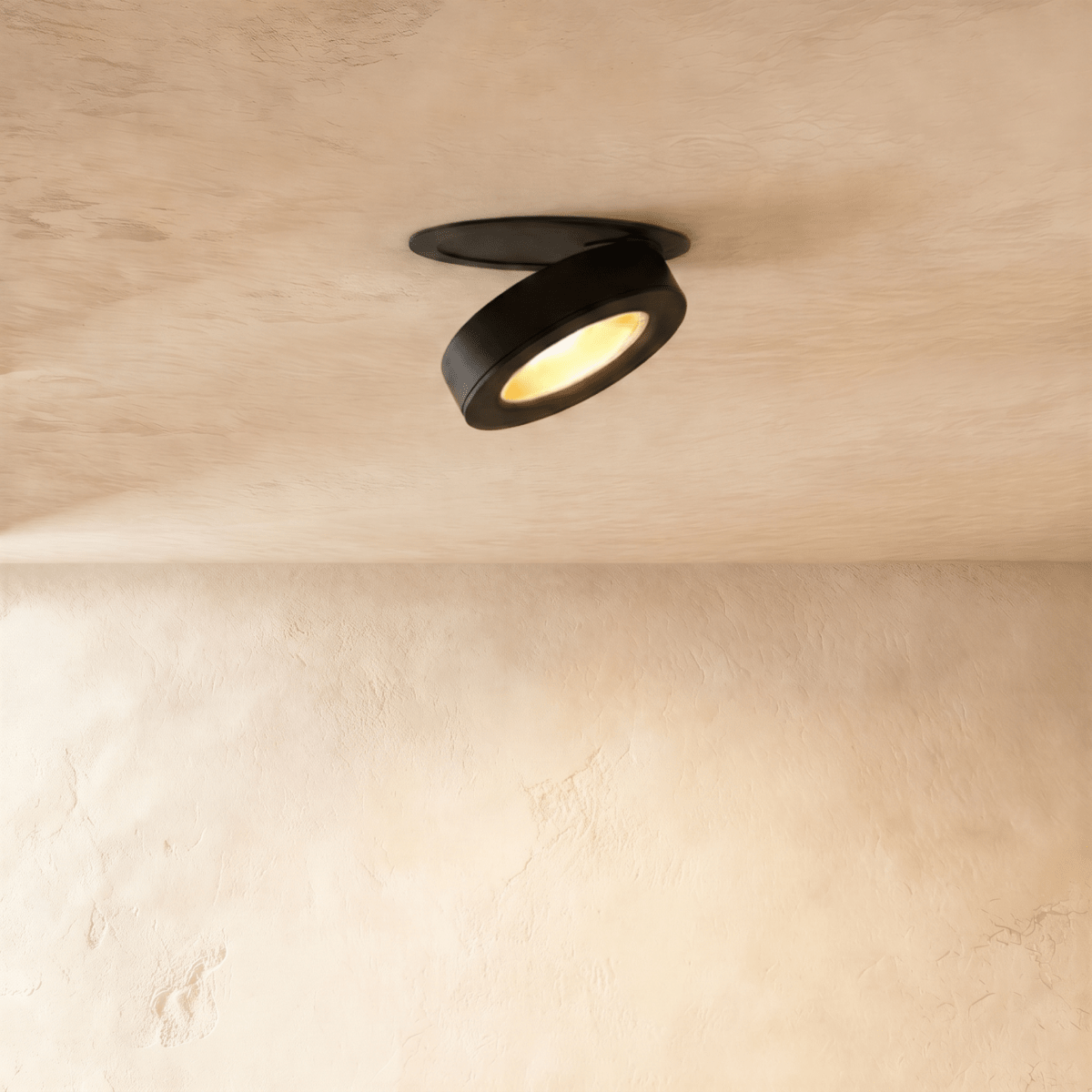 Clérachic recessed downlight in black, head swung down out of its ceiling plate and lit warm against a pale limewash ceiling.