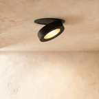 Clérachic recessed downlight in black, head tilted to a steeper angle and dropping a warm pool of light down the plaster wall below.