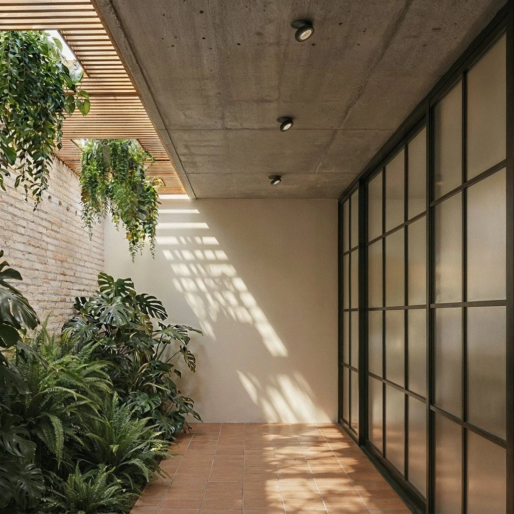 Clérachic recessed downlights in black, three units set into a concrete soffit above a tiled courtyard with brick planting beds and glazed doors.
