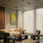 Clérachic black linear recessed downlights spaced across a concrete ceiling above a cream sofa and sheer curtains.
