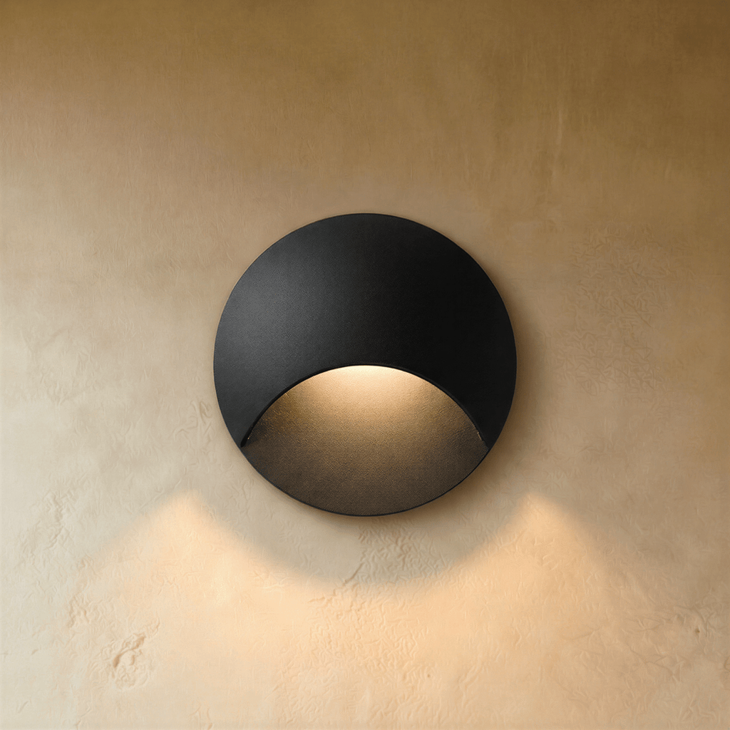 Clérachic recessed step light in matte black with a crescent-cut face, warm glow washing down a plaster stairwell wall.