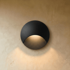 Clérachic recessed step light in matte black with a crescent-cut face, warm glow washing down a plaster stairwell wall.