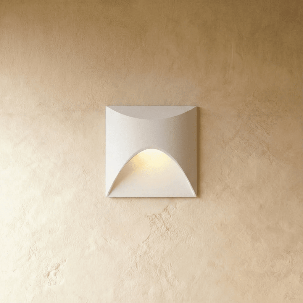 Clérachic recessed step light in white with a square face and arched cutout, warm glow spilling onto a plaster wall.