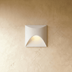 Clérachic recessed step light in white with a square face and arched cutout, warm glow spilling onto a plaster wall.