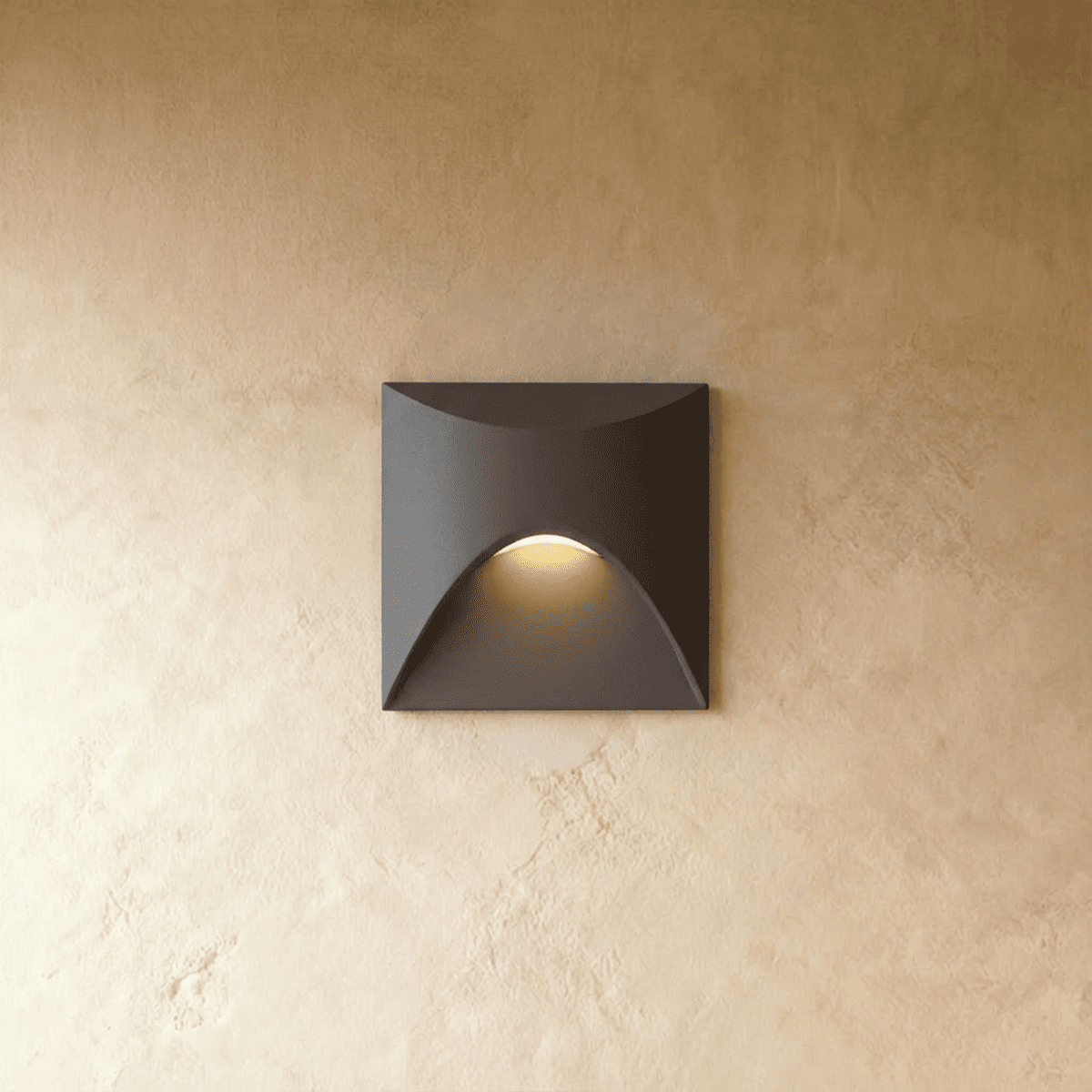 Clérachic recessed step light in matte black with a square face and arched cutout, warm glow spilling onto a plaster wall.