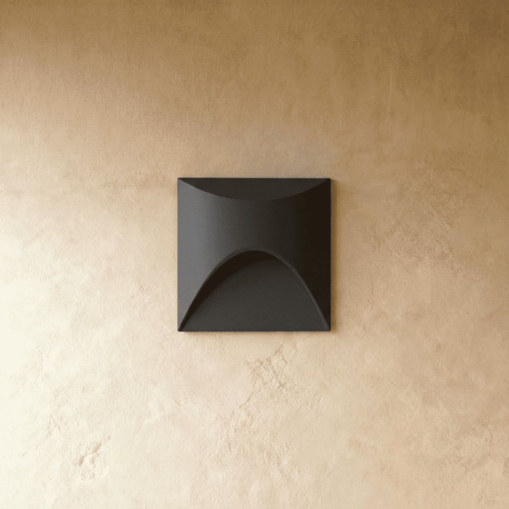 Clérachic recessed step light in matte black with a square face and arched cutout, shown unlit on a plaster wall.