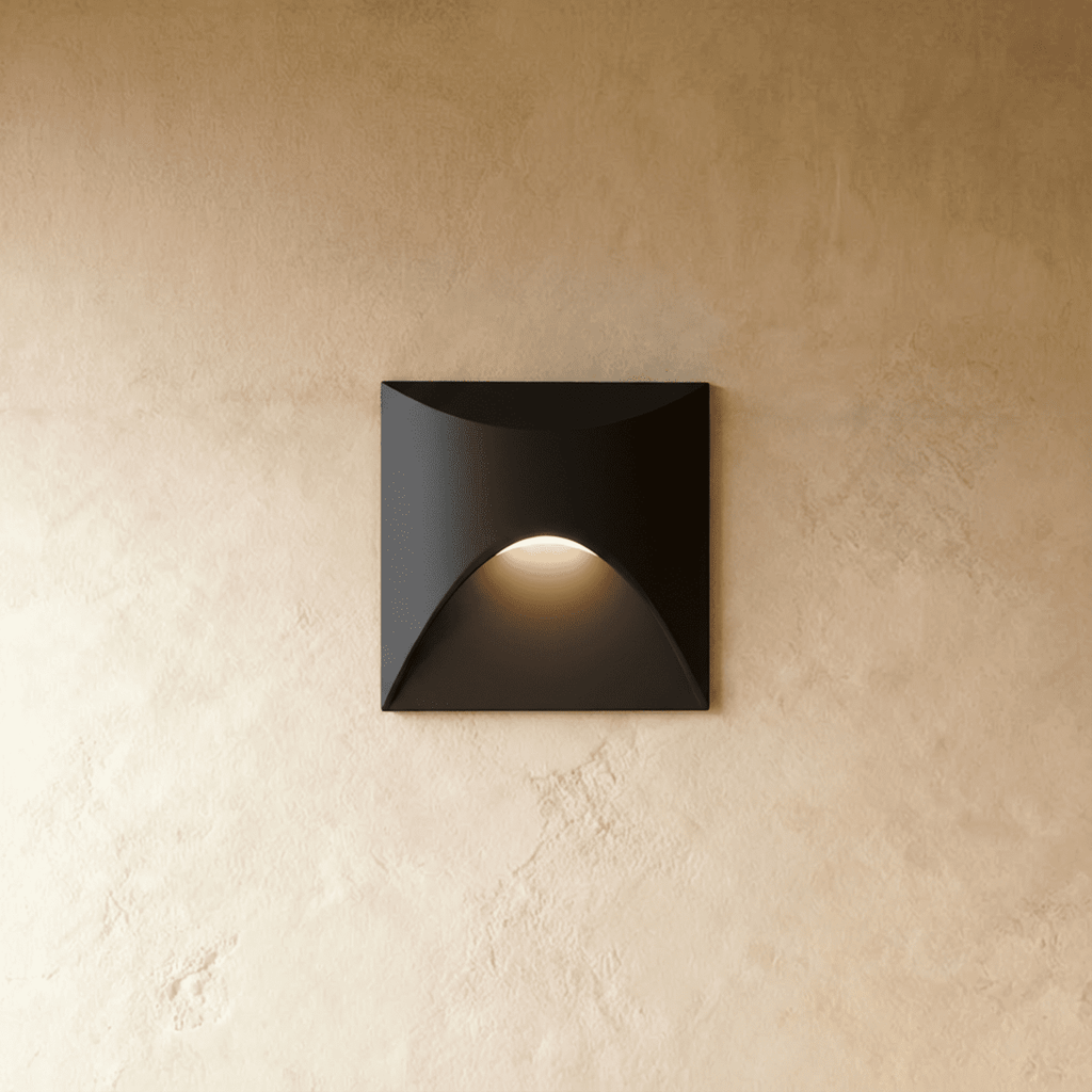 Clérachic recessed step light in matte black with a square face, warm light glowing softly from its arched cutout.