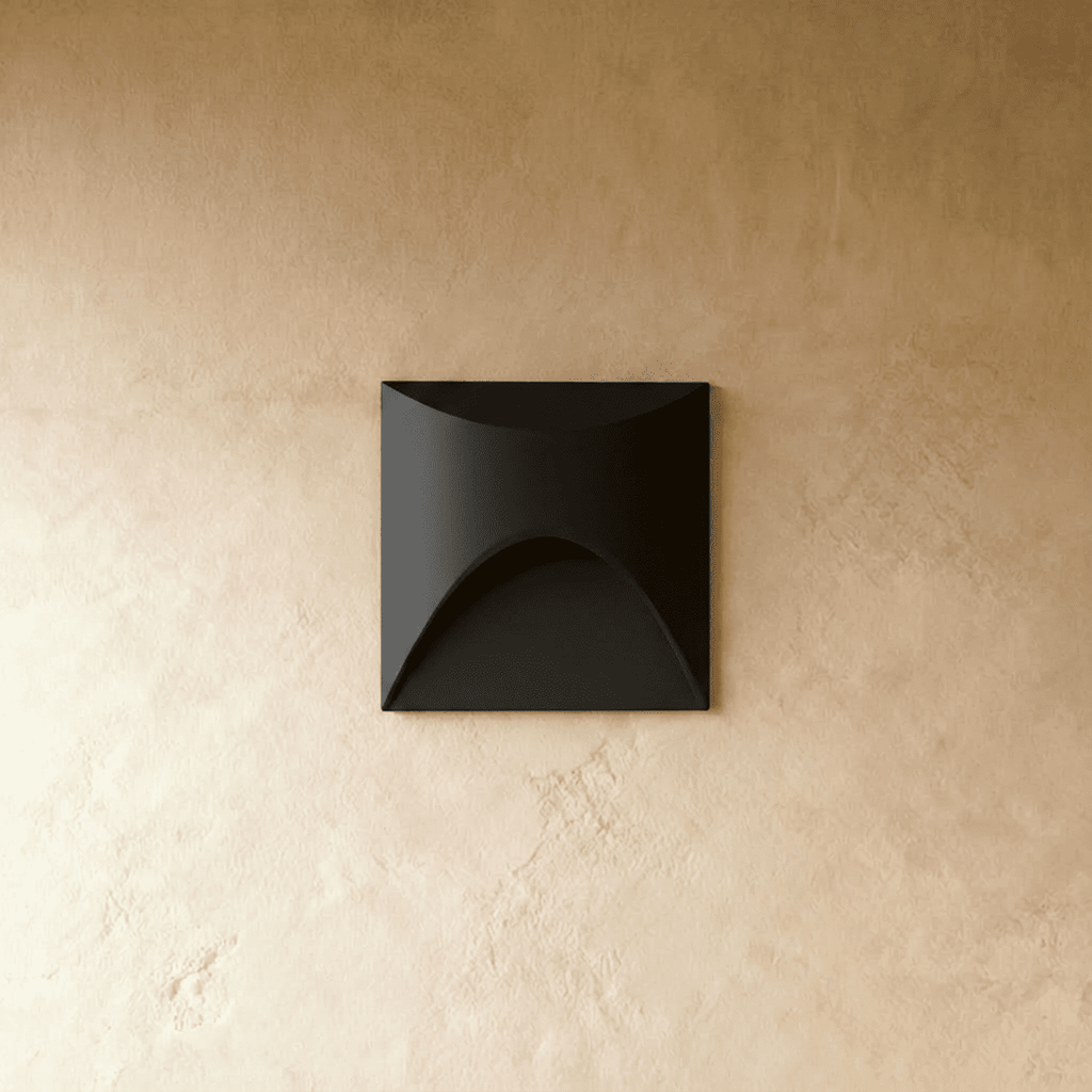 Clérachic recessed step light in matte black with a square face and arched cutout, seen unlit against a plaster wall.