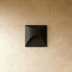 Clérachic recessed step light in matte black with a square face and arched cutout, seen unlit against a plaster wall.