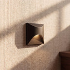 Clérachic recessed step light in matte black with a square face, warm glow lit close against a woven wall covering.