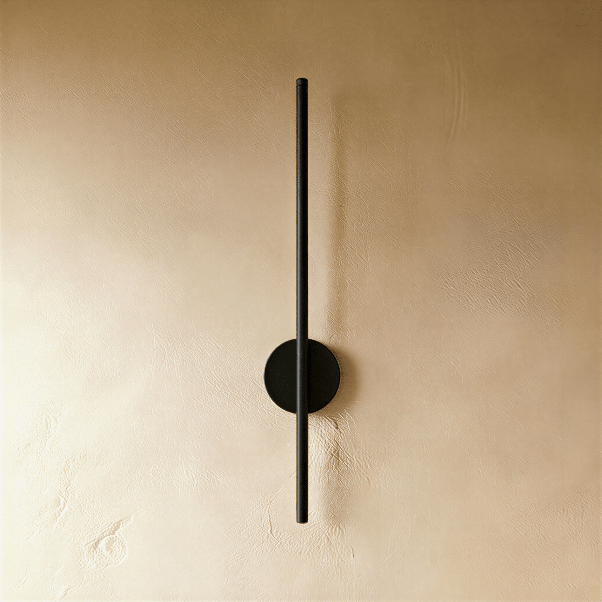 Clérachic slim black vertical wall lamp with a round backplate, switched off against a warm textured plaster wall.