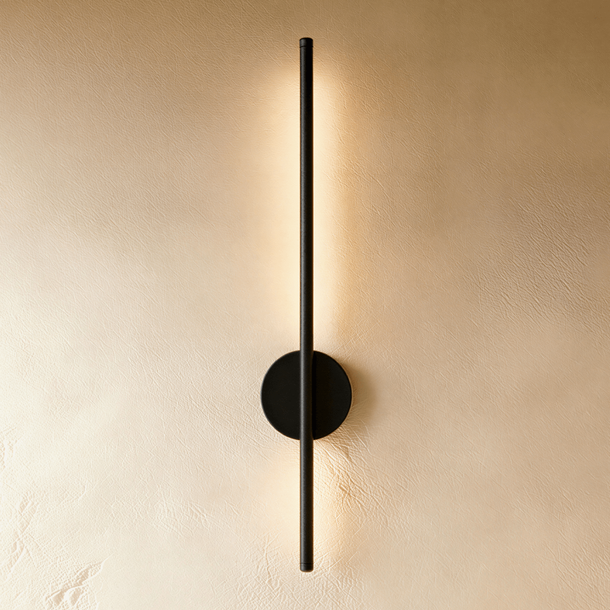 Clérachic taller slim black vertical wall lamp with a round black backplate, lit warm on a cream limewash wall.