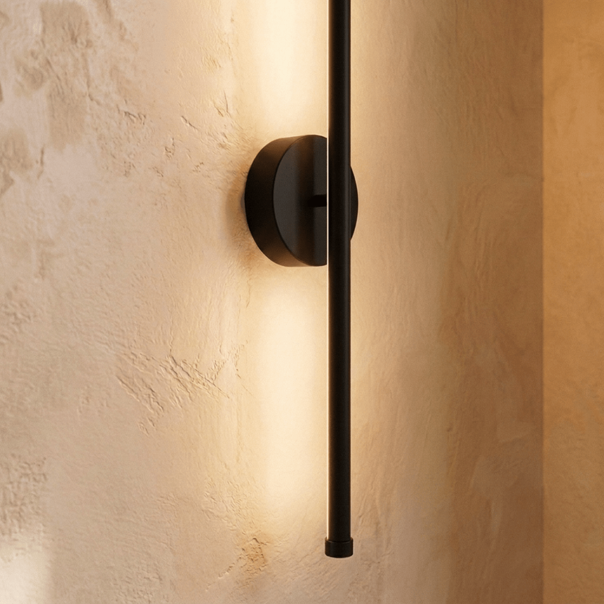 Close-up of the Clérachic black wall lamp, its round backplate and rod end with warm light spreading on plaster.