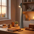 The grey Clérachic cone lamp lit on the same desk, warm light falling across the timber top.