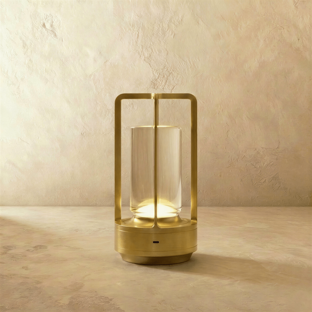 Clérachic brass table lamp: an open metal frame around a clear glass tube, glowing warm on a limewash-textured backdrop.