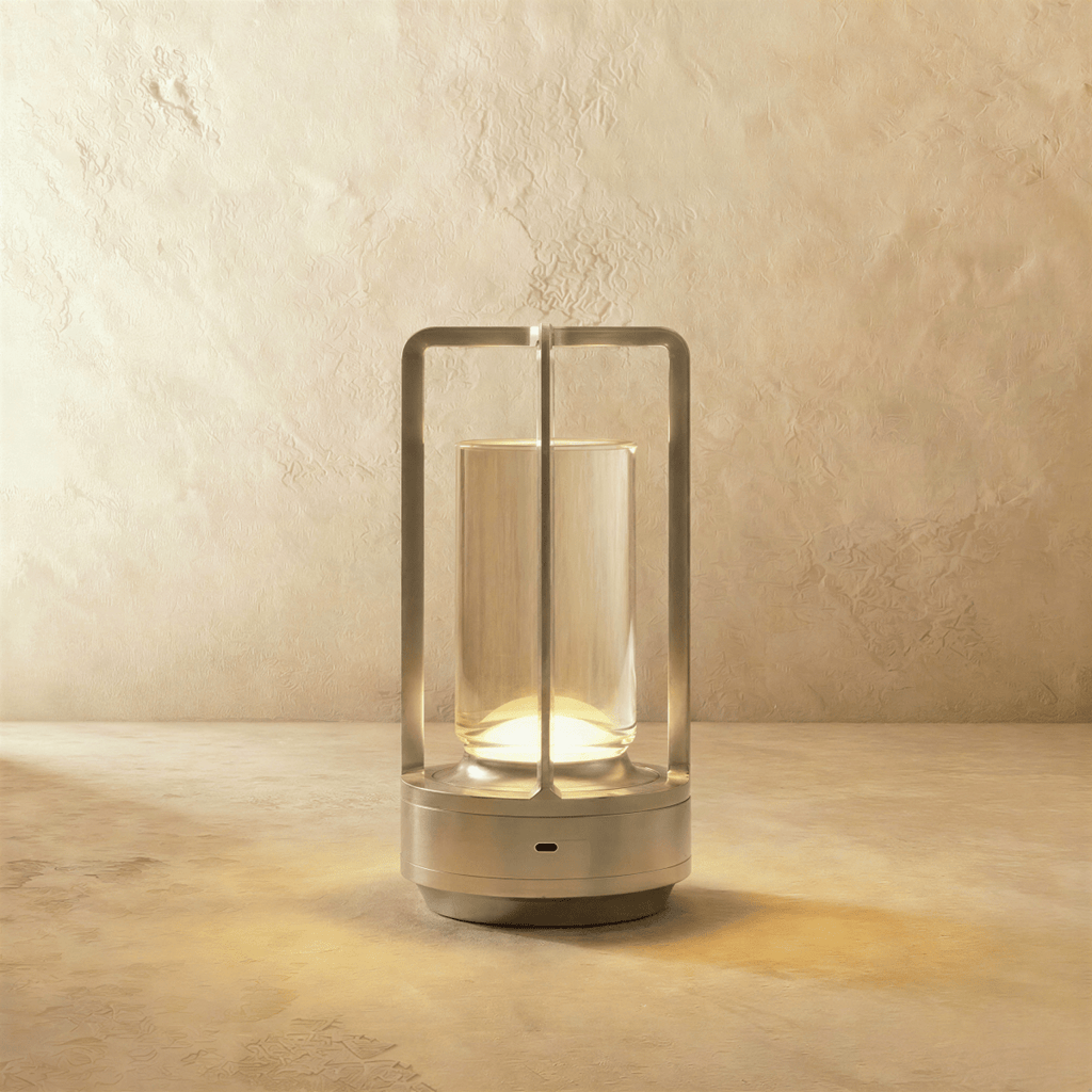 Clérachic silver-finish table lamp with an open frame and clear glass tube, lit warm on a pale limewash wall and stone surface.