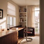 Clérachic small black table lamp on a walnut desktop by a sunlit window, with books, a roman blind and a chrome chair nearby.