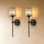 Clérachic pair of black wall sconces with fluted glass shades, lit warm and mounted side by side on a plaster wall.