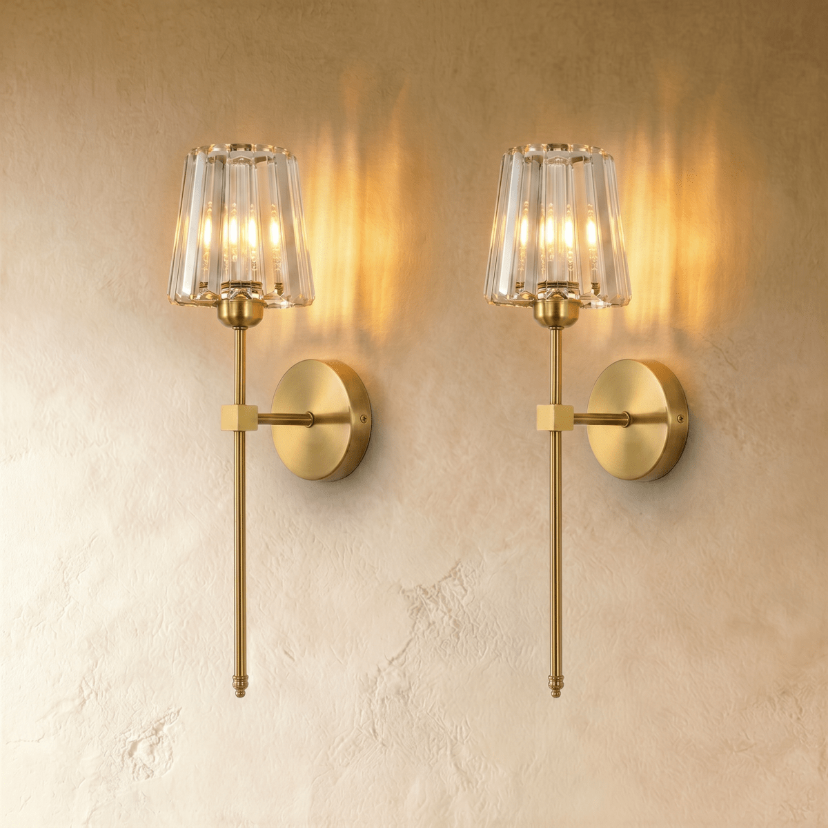 Clérachic pair of brass-gold wall sconces with faceted glass shades, glowing warm side by side on a plaster wall.