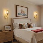 Clérachic pair of gold wall sconces with glass shades flanking a framed print above a bed in a cream bedroom.