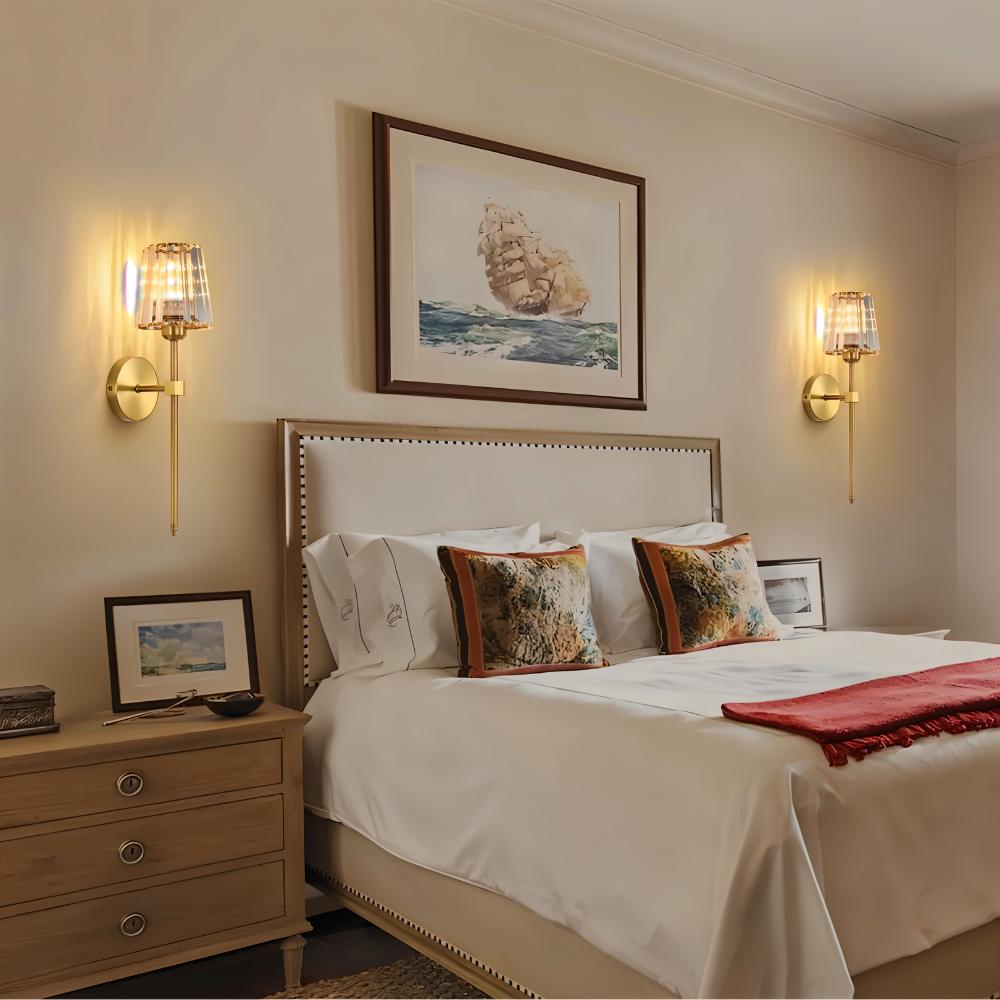 Clérachic pair of gold wall sconces with glass shades flanking a framed print above a bed in a cream bedroom.