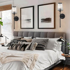 Clérachic pair of black wall sconces with fluted glass shades above a grey upholstered bed between two framed prints.
