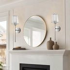 Clérachic pair of silver wall sconces with clear glass shades either side of a round mirror above a white mantel.