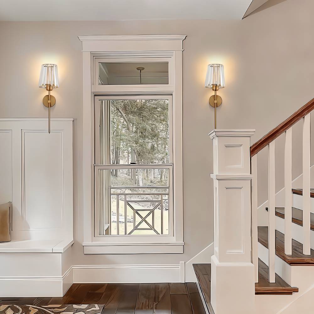 Clérachic pair of brass-gold wall sconces with glass shades either side of a tall white-framed window in a hallway.