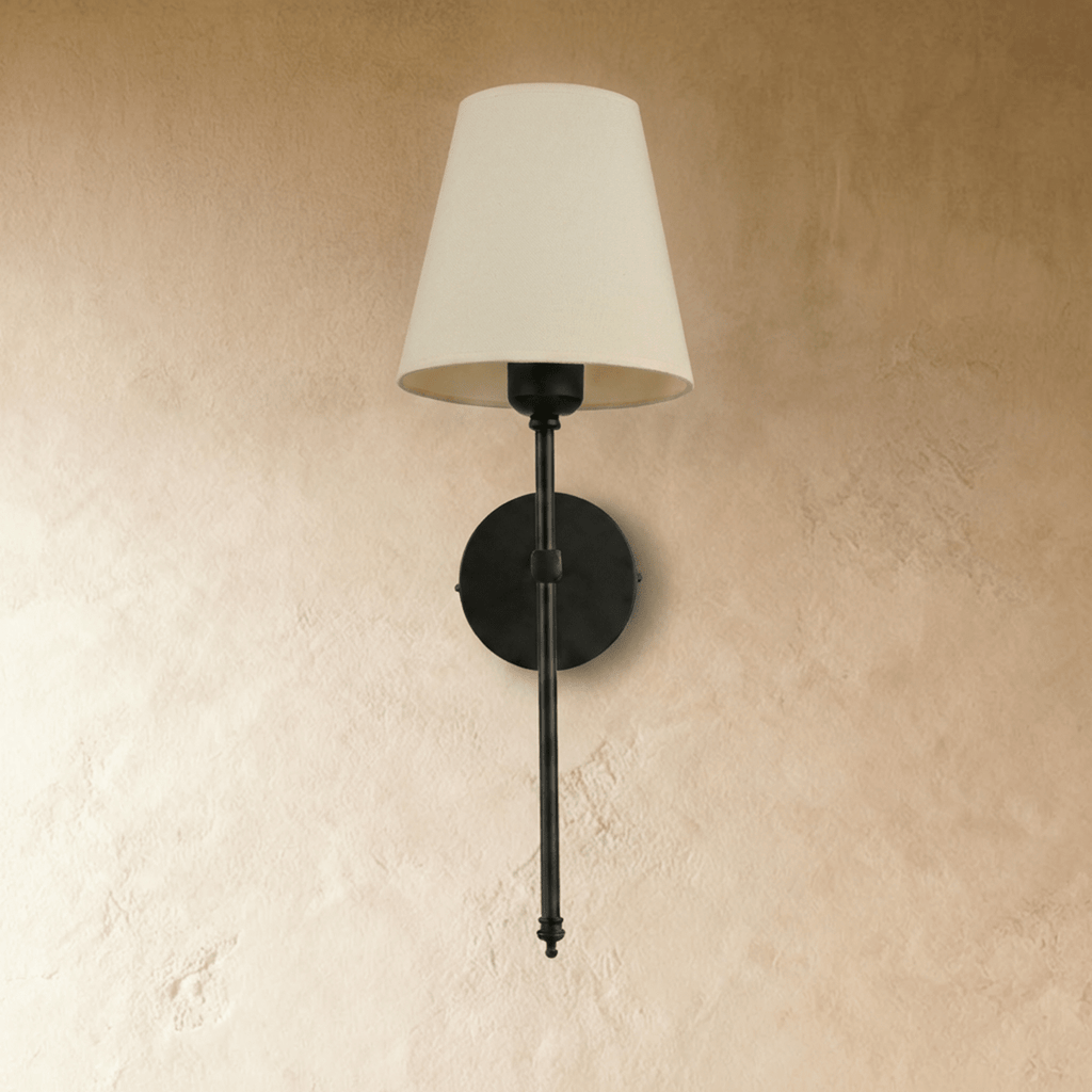 Clérachic black wall sconce with a cream tapered fabric shade on a slim rod, switched off against a plaster wall.
